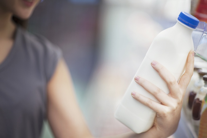 Woman checking label on milk in supermarket dairy section