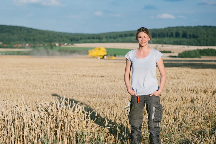 female farmer standing in the wheat field, combine harvester in the background