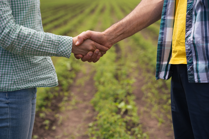 The deal is on. Two farmers shaking hands on an agricultural field background. Getting to an agreement that is mutually beneficial. Business casual greeting handshake.